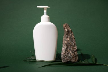 Samimi jel ya da duş kremi olarak kullanılabilecek temiz, beyaz, boş bir maket şişesiyle dolu bir hayat, palmiye yaprağının üzerindeki kayanın yanında, yeşil stüdyo arka planında izole edilmiş. Marka paketi. Reklam alanını kopyala