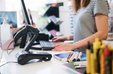 Ofis gereçlerinde bilgisayar bilgisayarı olan bir tezgahın yanında duran bir satıcının bulanık arka planındaki barkod tarayıcısı ve POS terminali veya kredi kartı okuyucusuna seçici odaklanma. Halk ve ticaret