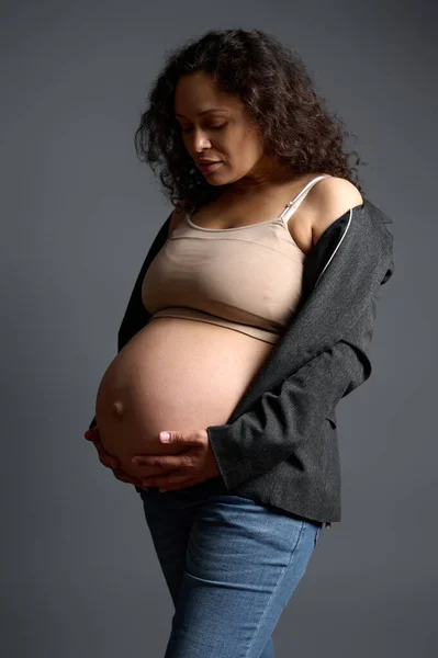 迷人的孕妇轻轻地抚摸着她的大肚子 体验着美妙的情感 感受着婴儿的动作 孤立的灰色背景 无忧无虑的怀孕快乐母性 身体呈阳性女性气质 — 图库照片
