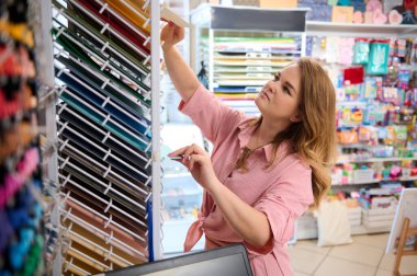 Güzel sanatlar, yaratıcılık, pastel ve suluboya çizimler için renkli kağıtları seçen çekici genç bir kadın tasarımcı veya yaratıcı bir sanat mağazasında karton çarşaflar düzenleyen bir satıcı.