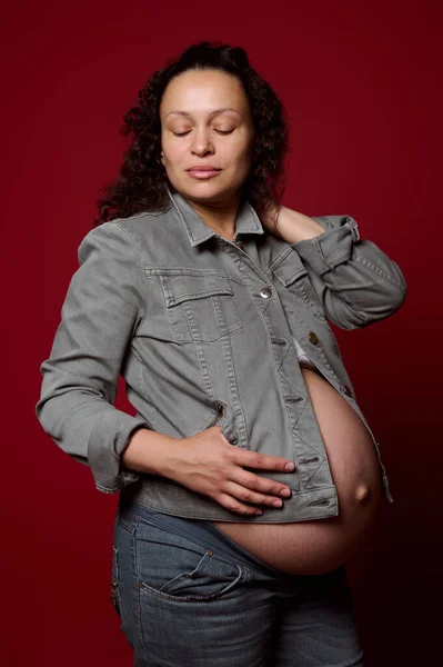 多种族的孕妇 穿着休闲装的准妈妈 紧盯着红色孤立的工作室背景 摆出一副若有所思的样子 怀孕36周 产妇生活方式 — 图库照片