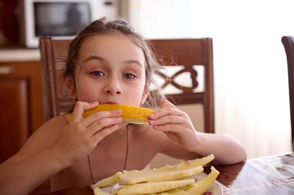 Piękna Dziewczynka Jedząca Pyszne Melony Siedząca Przy Stole Domowej Kuchni — Zdjęcie stockowe