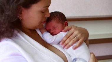 Onu kucaklayan, öpen ve sallayan şefkatli annesinin kollarında uyuyan sevimli yeni doğmuş bebeğinin yakın çekimi. Hamilelik, annelik, doğum ve çocuk bakımı kavramı. - İnsanlar. Yaşam biçimi