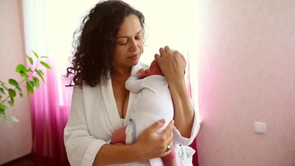 美丽的拉丁美洲女人 疼爱着抱着和摆动着新生婴儿的慈母 亲吻着他 表达着快乐而积极的情感 关心和柔情 站在家里的卧室里 — 图库视频影像