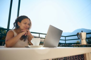 Çok ırklı otantik orta yaşlı kadın dizüstü bilgisayar ekranına bakıyor, yeni iş projesini düşünüyor, ev terasında masada oturuyor, millet. İş için. Açılış