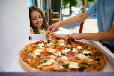 Küçük mutlu bir kız, Napoli usulü İtalyan Margherita pizzasıyla karton bir kutuya bakıyor, taze pişmiş ve çıtır çıtır. İtalyan mutfağı, kültürü ve gelenekleri