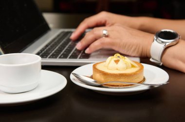 Lezzetli bir Fransız tatlısının yakın çekimi, dizüstü bilgisayarda yazı yazan bayanların arka planında limon kremalı tart. Yiyecek ve içecek. İnternet işi. Uzak çalışma