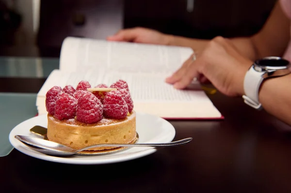 Kitap okuyan bir kadının arka planında bir ahududu tartı. - İnsanlar. Yiyecek tüketimi. Fransız pastanesi. Yaşam biçimi