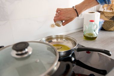 Bir adamın elinin tabağa baharat katarken yakın plan çekimi, evde yemek pişirirken körfez yaprağı ve zeytinyağı ile kızartma tavasına biber koymak. Mutfak. Mutfak. Sağlıklı beslenme. Diyet