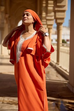 Çok güzel bir Müslüman kadının portresi tesettür takıyor mermer sütunların arasında dikiliyor, turuncu Orijinal kıyafetler giyiyor. İslami Arap modası. Zarafet. - İnsanlar. Din