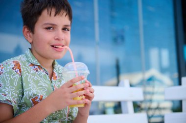 Yakışıklı, tapılası İspanyol bir çocuğun portresi. Smoothie içiyor, kameraya bakıyor, açık bir kafede oturuyor.