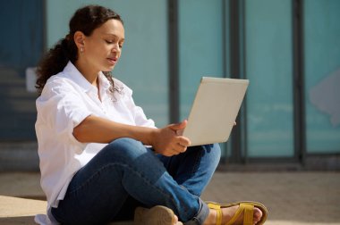 Üniversitenin kendine güvenen genç bayan öğrencisi açık havada oturuyor ve diploması için online proje yapıyor. - İnsanlar. - İnternet. Eğitim. - Bilgi. Kariyer ve adam toplama konsepti. Boşluğu kopyala