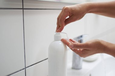 Yakın plan bir kadının eli, ellerini yıkarken sıvı sabun sıkarken beyaz ev banyosunda lavabonun yanında dikilirken. Temizlik ve hijyen konsepti. Sağlıklı bir yaşam tarzı. Antiseptik temizlik ürünü kullanarak.