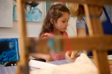 Sanat atölyesinde ya da sanat galerisinde resim ve resim öğrenen küçük şirin bir kızın bulanık ahşap bir sehpası olsa da beyaz bir arka planda boyalı resimler sergilenmektedir. - İnsanlar. Güzel sanatlar