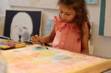 Resim çizen sevimli bir kızın yakın plan portresi, yaratıcı sanat atölyesinde masa başında oturuyor. Çocuk eğlencesi ve sanatsal beceriler, ilham ve hayal gücü gelişimi. Görsel sanat