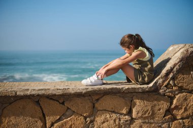 Kafkasyalı şirin küçük bir kızın tam boy portresi taştan bir korkulukta oturmuş, rüya gibi bir şekilde okyanus fırtınasına hayran bakıyordu. - İnsanlar. Boş zaman aktivitesi. - Aile. Çocuklar işte. Aktif sağlıklı yaşam tarzı