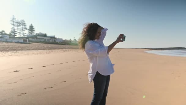 身着休闲装的女人站在大西洋边的沙滩上 用她的智能手机拍下了海浪冲撞海岸的照片 旅游和探险 — 图库视频影像