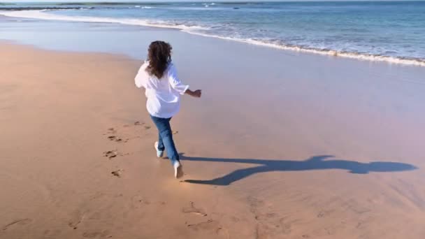 Счастливая Женщина Джинсах Бегает Песчаному Пляжу Оборачивается Выражает Позитивные Эмоции — стоковое видео