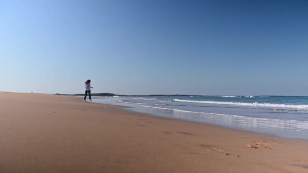 年轻的卷发多民族妇女穿着蓝色牛仔裤和白衬衫 在一个阳光灿烂的秋日沿着沙滩奔跑 健康积极的生活方式 人与自然 室外娱乐活动 — 图库视频影像