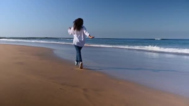真实的女人在沙滩上奔跑 在潮湿的沙滩上留下脚印 海浪涌向她的脚 Sher转身感到快乐和自由 — 图库视频影像