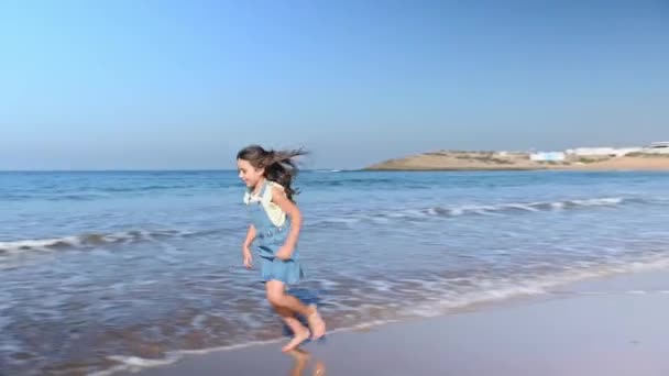 白种人小女孩赤脚在美丽的沙滩上奔跑 在阳光灿烂的日子里享受户外散步 快乐的孩子喜欢海浪拍岸 喜欢隐藏她奔跑时留下的脚印 — 图库视频影像