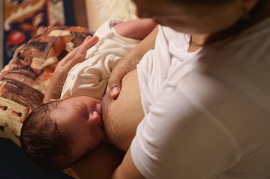 Sevgi dolu bir annenin bebeğini sağlıklı beslenmesi oturma odasındaki kanepede oturmasının özgün bir portresi. Sağlıklı beslenme ve evde sağlık kavramı..