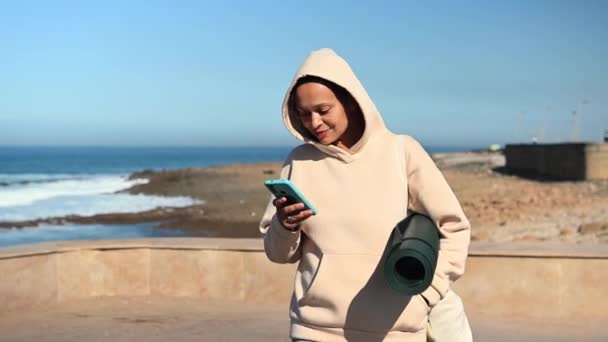 Glad Multietnisk Ung Vuxen Kvinna Sportkläder Använder Smart Mobiltelefon Ler — Stockvideo