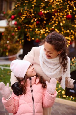 Otantik neşeli aile, çoklu etnik anne ve küçük kız gülümsemesi, birlikte mutlu kış tatilleri, geleneksel aile pazarında aydınlatılmış Noel ağacı ya da Noel panayırında ayakta durmak