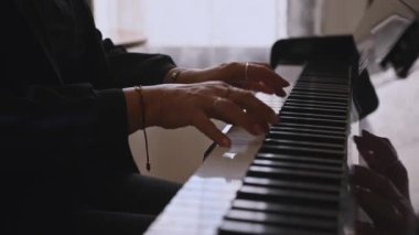 Siyah giyinmiş tanınmayan bir kadın piyanistin yakından görünüşü, piyano çalarken parmaklarını piyano tuşlarına koyması, klasik müziğin performansının keyfini çıkarması. Yavaş çekim