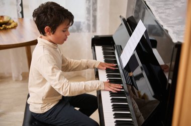 Koyu renk saçlı, sevimli çocuk müzik dersinde piyano çalıyor. Yakışıklı küçük piyanist bir müzik bestecisi, akor enstrümanında öğreniyor - piyano -