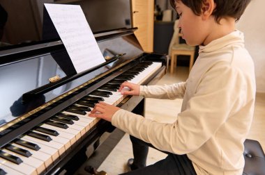 Yakışıklı melez genç okul çocuğu, günlük kıyafetler içinde, evde müzik öğreniyor, büyük piyano çalıyor. - İnsanlar. Eğitim. Sanat, kültür ve eğlence.