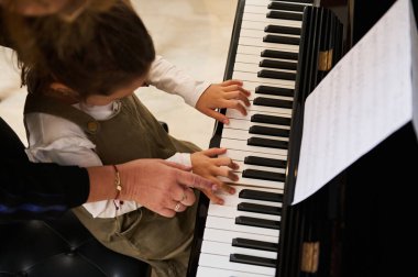 Üst düzey müzik öğretmeni, küçük bir kızın elini tutan piyanist, öğrenciye piyano dersi veren, ona doğru parmak pozisyonunu gösteren. Çocuk eğitimi, sanatsal beceriler geliştirme