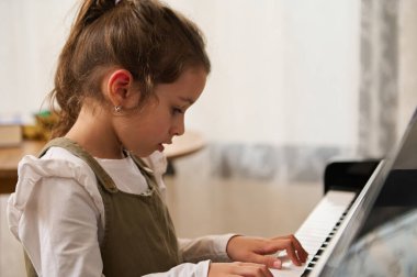 Güzel ilkokul çocuğu, küçük piyanist piyano çalıyor ve içeride şarkı söylüyor. Yetenekli çocuk müzisyen müzik ve şarkı yaratır, piyano çalar, bir melodi besteler. Akort enstrümanı üzerinde çalışıyorum.