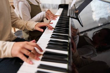 İki çocuğun yakın çekimleri. Büyük piyanoda müzik çalan kız ve erkek. Çocuklar parmaklarını abanoz ve fildişi tuşlara basıyor. Müzik dersi