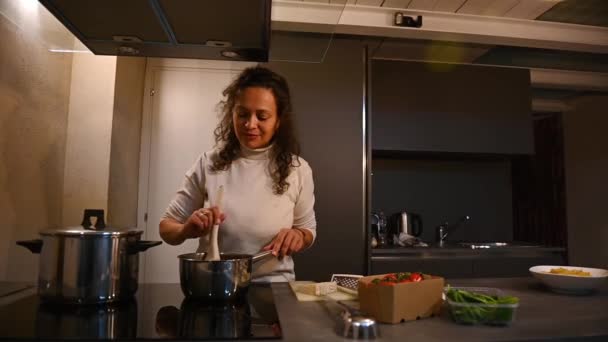 漂亮的女人站在厨房柜台边的电炉旁 品尝着她在平底锅里搅拌的番茄酱 用手做着好吃的标志 贝尔利西莫边做饭边说 — 图库视频影像