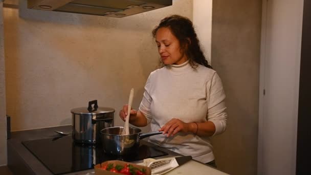迷人的家庭主妇让好吃的好好吃好高兴的手签 亲亲手指尝番茄酱 站在电炉边 用平底锅搅拌配料 在家里厨房做饭 — 图库视频影像
