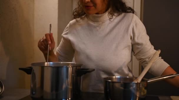 特写可爱的家庭主妇站在厨房的火炉边 一边在平底锅里搅拌水 一边做意大利法式法式面食 女厨师通过浪漫的灯光准备晚餐 — 图库视频影像