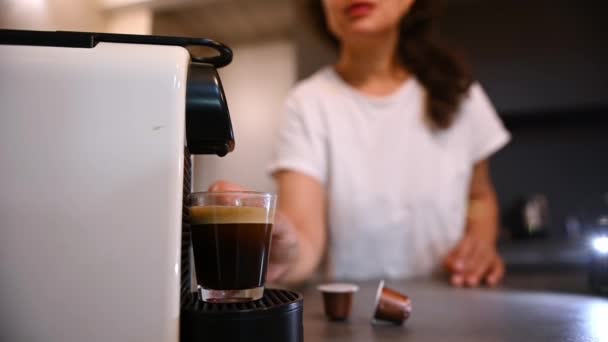 在一个身穿白色睡衣的黑发女人的模糊背景下 有选择地把注意力集中在家用咖啡机上 一边喝着新鲜酿制的浓缩咖啡 一边在家里享用着早晨的咖啡 — 图库视频影像