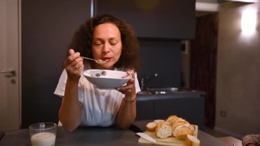 Ağır çekim. Çoklu etnik kıvırcık saçlı, genç, yetişkin esmer, büyüleyici düşünceli kadın sabahları kahvaltısını süt ile yiyor, rüya gibi bakışlar atıyor, mutfak tezgahının yanında duruyor.