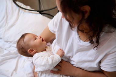 Kıvırcık, esmer, genç bir kadının özgün portresi mutlu, sevgi dolu bir anne gülümseyen, pozitif duygular ifade eden, yeni doğmuş bebeğini emziren ve kucaklayan. - İnsanlar. Doğum izni yaşam tarzı.