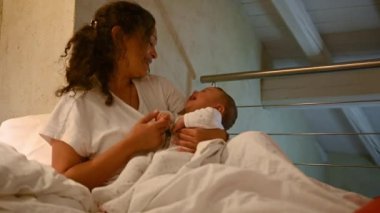 Sevimli küçük oğlan, onunla konuşan, gülümseyen, şefkatle kucaklayan ve sabah kalktıktan sonra yatakta oturan annesinin kollarında güler. Bebek ve bebek bakımı