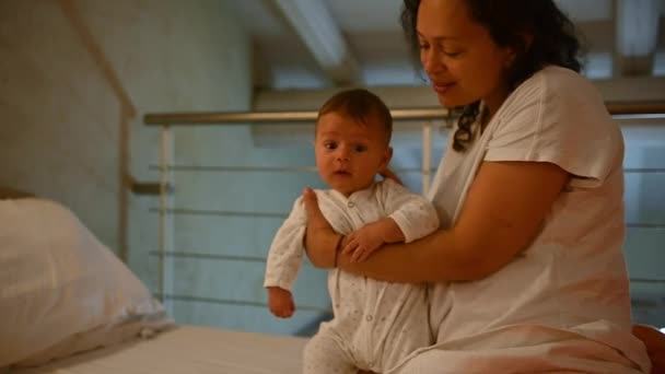 慢动作充满爱心的充满爱心的拉丁美洲母亲抱着 亲吻和拥抱她可爱的新生男婴 坐在舒适的卧室里的床上 幼儿保育 — 图库视频影像