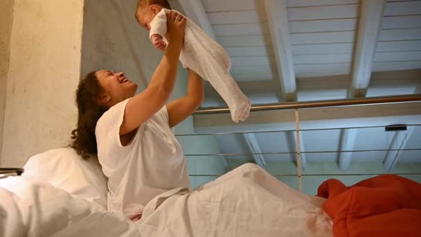 可爱的母亲坐在床上 早上和心爱的男婴玩耍 美丽的多民族妇女享受着她的母性生活方式 与新生婴儿有联系 母亲和幼儿 — 图库视频影像