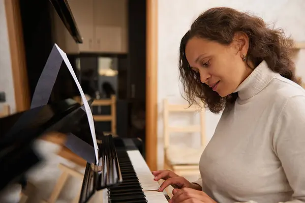 Authentic multiracial young woman pianist playing grand piano and singing song. Talented female composer musician creates music, performs on pianoforte, composes melody, practices on chord instrument