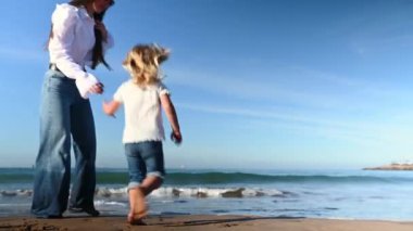 Neşeli genç anne küçük kızıyla oynuyor, Atlantik sahilinde yalınayak koşuyor, dalgaların üzerinde zıplıyor kıyıya çarpıyor, birlikte mutlu bir hafta sonu geçiriyorlar.
