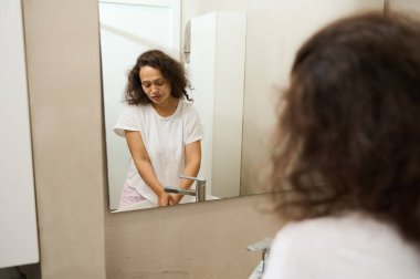 Banyoda seramik lavabonun önünde duran güzel bir kadın musluğun altında akan suyla ellerini sabunla yıkıyor. Vücut bakımı ve hijyen kavramı