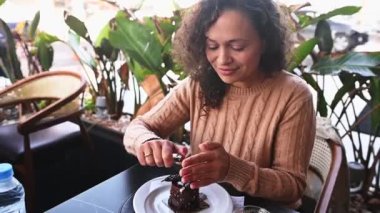 Gülümseyen esmer kadın, doğum günü pastasında mum yakan bir doğum günü kızı, açık havada güzel bir kafede doğum gününü kutluyor. - İnsanlar. Yaşam tarzı. Mutlu yaşam olayları