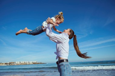 Mutlu şefkatli genç anne ve tatlı kızı kumsalda birlikte oynuyorlar.