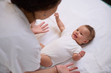 Sevimli beyaz oğlan 4 aylıkken yatakta uzanıyor, kollarını açık tutuyor, annesine gülümsüyor. Yukarıdan bak. Bebeklik. Bebeklik. Doğum izni konsepti. Mutlu aile ilişkileri.