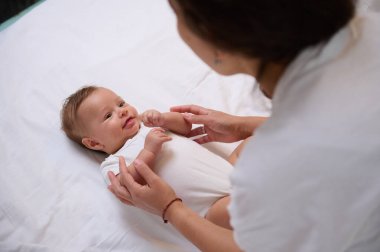 Sevgi dolu bir annenin bebeğine sarılışının görüntüsü. Yeni doğmuş çocuğuna bakan, altını değiştiren, ayak masajı yapan ve küçük, ince elleriyle ilgilenen genç bir anne. - İnsanlar. Doğum izni yaşam tarzı